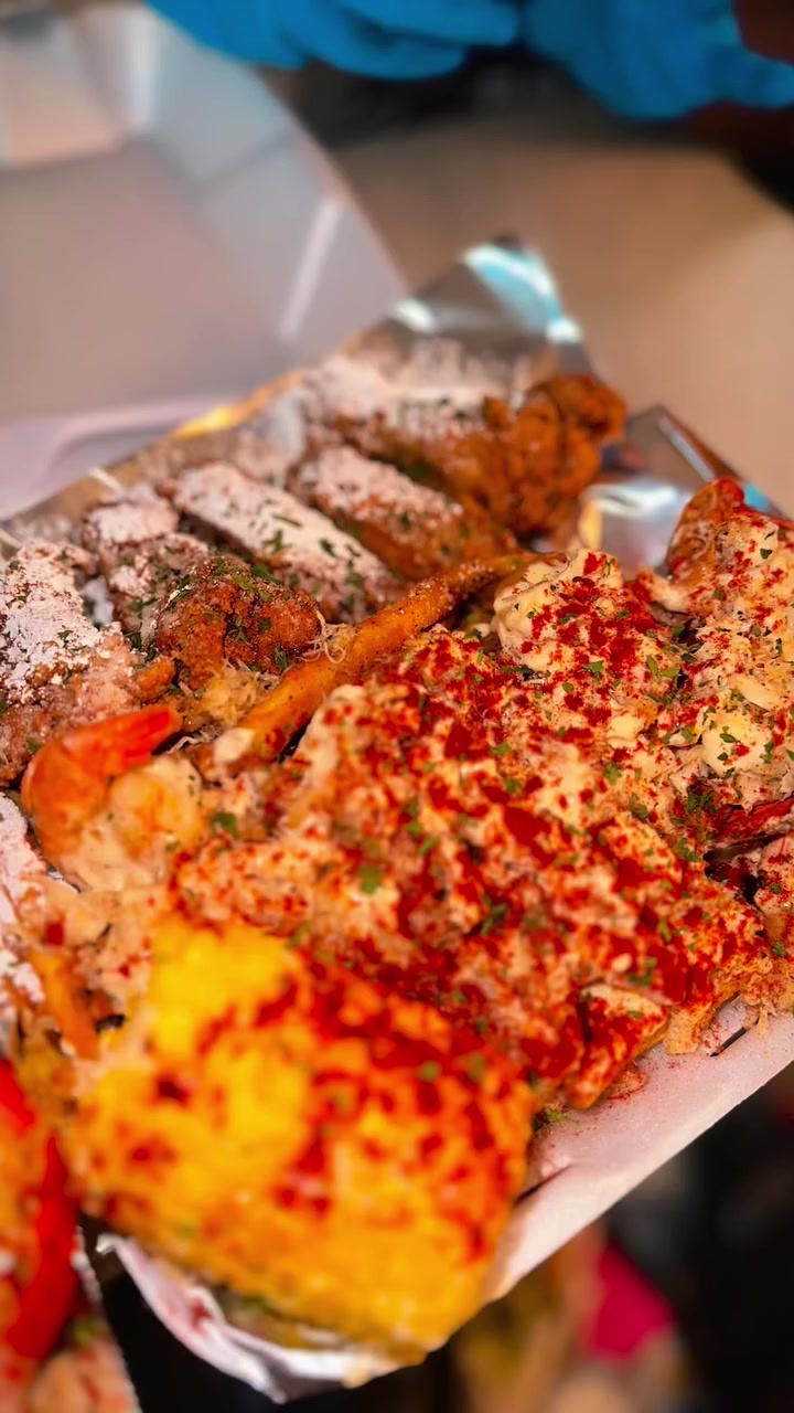 Foil tray of wings, shrimp, corn and seafood in seasoned butter sauce