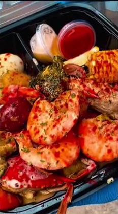 Takeout tray of seafood boil with shrimp, corn, broccoli, potatoes and dipping sauces